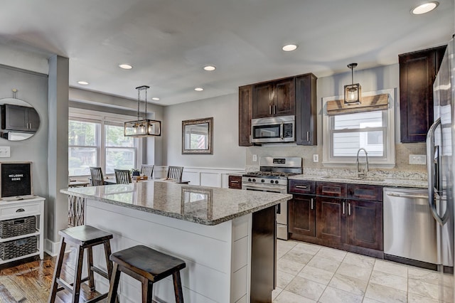kitchen featuring appliances with stainless steel finishes, a sink, light stone countertops, a breakfast bar, and a center island