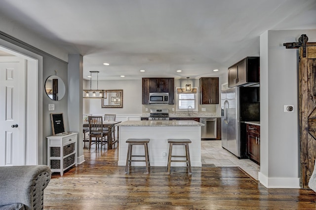 kitchen featuring stainless steel appliances, dark brown cabinets, a kitchen island, recessed lighting, and light wood-type flooring