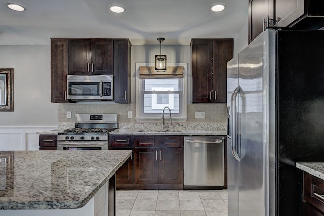 kitchen featuring appliances with stainless steel finishes, a sink, dark brown cabinets, light stone countertops, and recessed lighting
