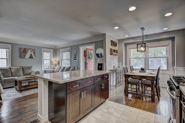 kitchen with open floor plan, stainless steel range with gas stovetop, light stone countertops, recessed lighting, and hanging light fixtures