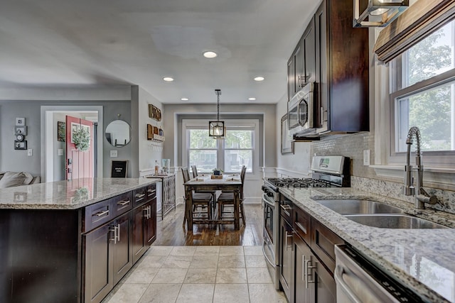kitchen with stainless steel appliances, a sink, decorative light fixtures, light stone countertops, and dark brown cabinetry
