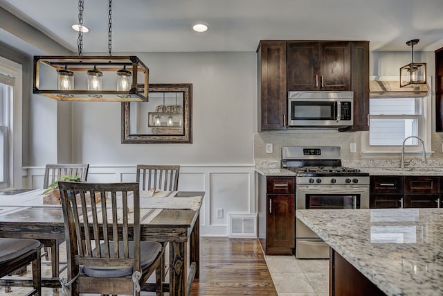 kitchen featuring stainless steel appliances, a sink, dark brown cabinetry, light stone counters, and a decorative wall