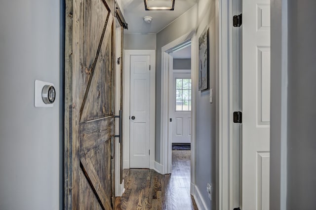 hallway with a barn door, dark wood-style floors, and baseboards
