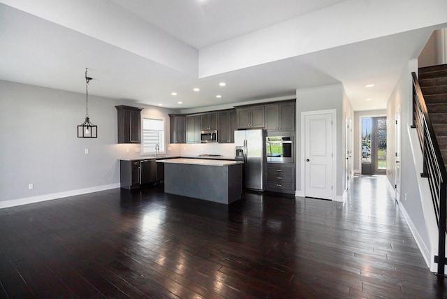 kitchen with appliances with stainless steel finishes, dark brown cabinets, baseboards, a center island, and dark wood-style floors