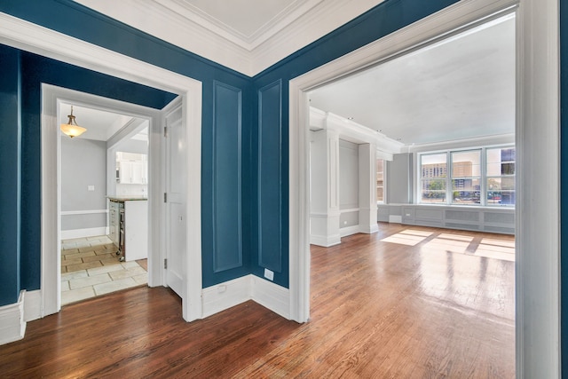 empty room featuring ornamental molding, a decorative wall, wood finished floors, and baseboards