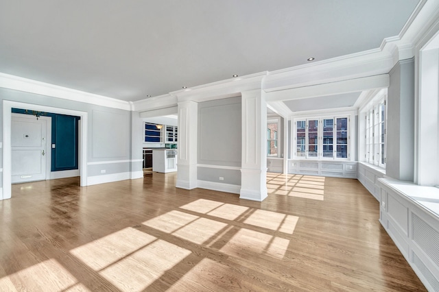 unfurnished room featuring ornamental molding, a decorative wall, ornate columns, and light wood-style flooring