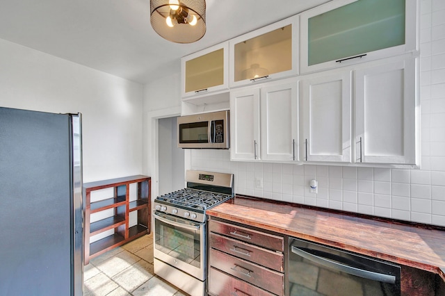 kitchen with appliances with stainless steel finishes, wood counters, backsplash, white cabinetry, and glass insert cabinets