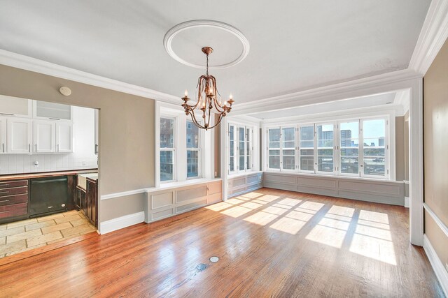 unfurnished dining area featuring a chandelier, crown molding, baseboards, and light wood-style flooring