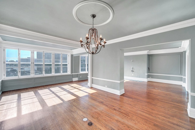 empty room with ornamental molding, a chandelier, baseboards, and wood finished floors