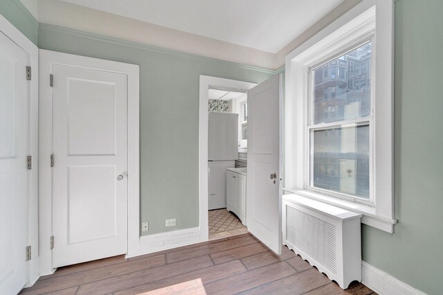 unfurnished bedroom with wood finished floors, freestanding refrigerator, radiator, baseboards, and ensuite bath
