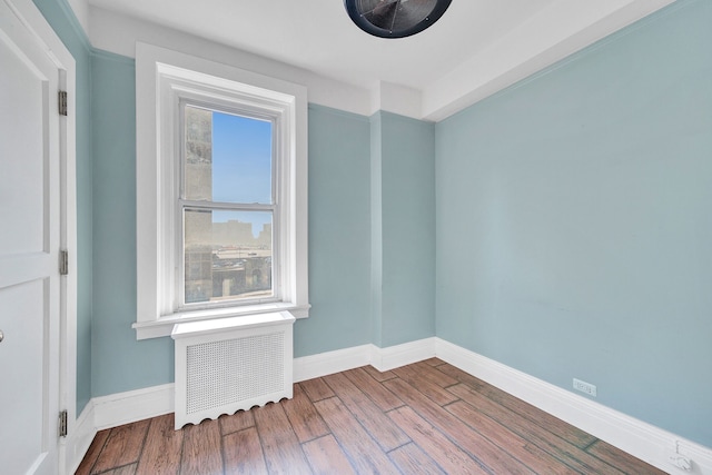 spare room with baseboards, wood finished floors, and radiator