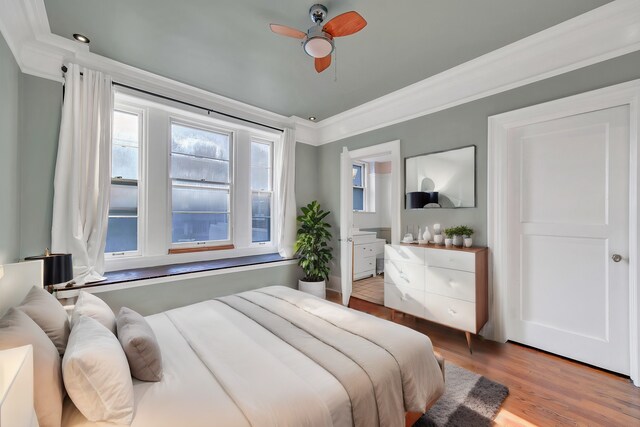bedroom with ornamental molding, multiple windows, wood finished floors, ceiling fan, and ensuite bathroom