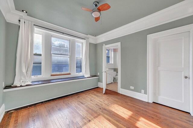 unfurnished bedroom featuring ornamental molding, baseboards, wood finished floors, ensuite bath, and a ceiling fan
