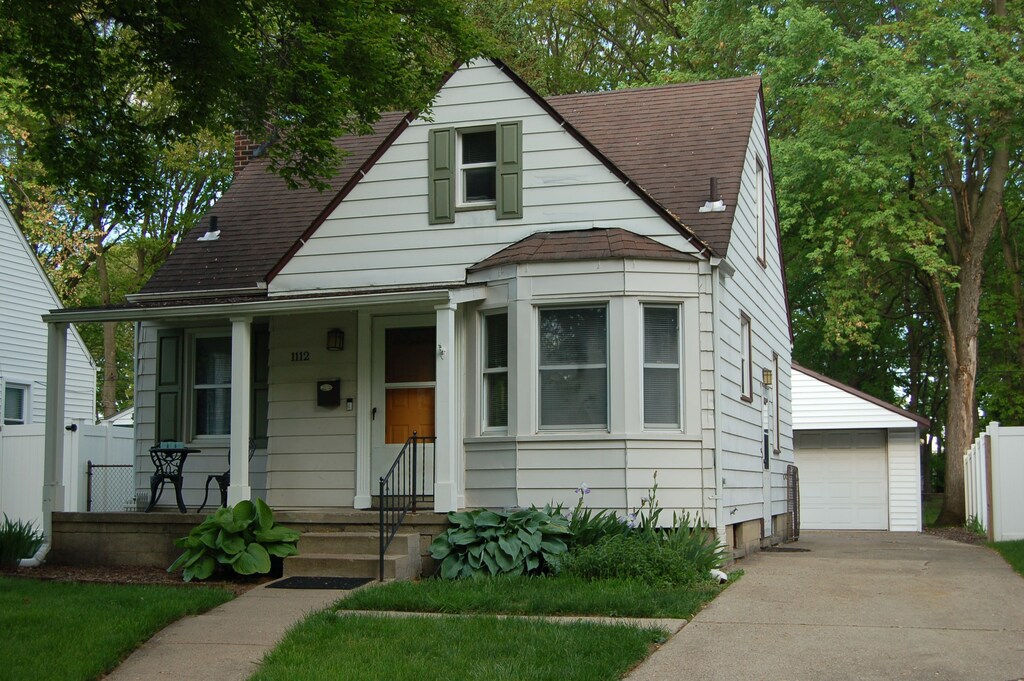 bungalow-style house with roof with shingles, an outbuilding, a porch, a detached garage, and a chimney