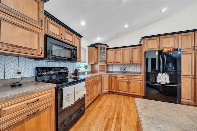 kitchen featuring black appliances, lofted ceiling, decorative backsplash, brown cabinetry, and light wood finished floors