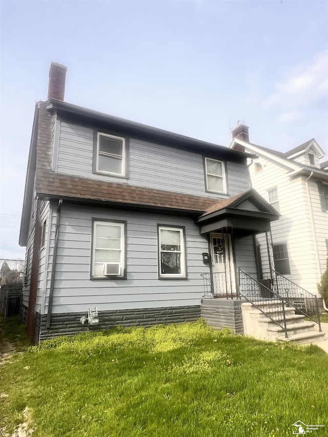 view of front facade featuring a front yard, a shingled roof, and a chimney