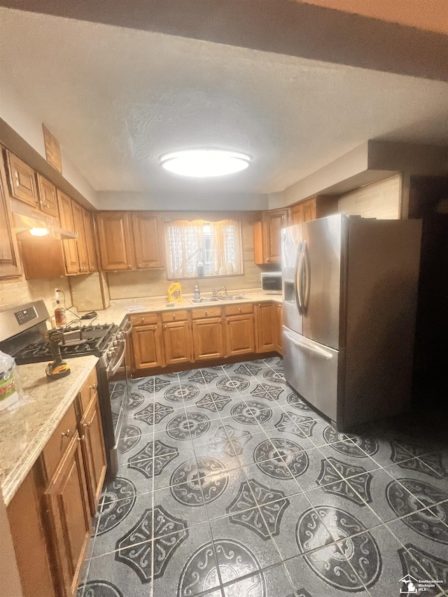 kitchen with stainless steel appliances, light countertops, a sink, light tile patterned floors, and a textured ceiling