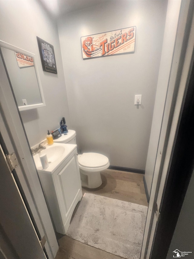 bathroom with vanity, toilet, wood finished floors, and baseboards