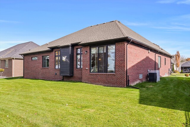 back of house with brick siding, a yard, cooling unit, and roof with shingles