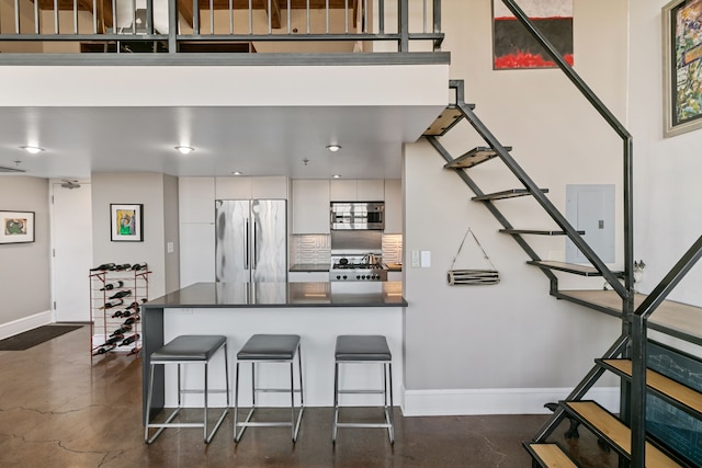3434 Russell St Unit 28-205, Detroit, MI 48207 - kitchen featuring appliances with stainless steel finishes, concrete floors, dark countertops, a kitchen bar, and baseboards