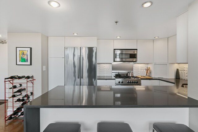 3434 Russell St Unit 28-205, Detroit, MI 48207 - kitchen featuring premium appliances, dark countertops, a peninsula, white cabinets, and a kitchen bar