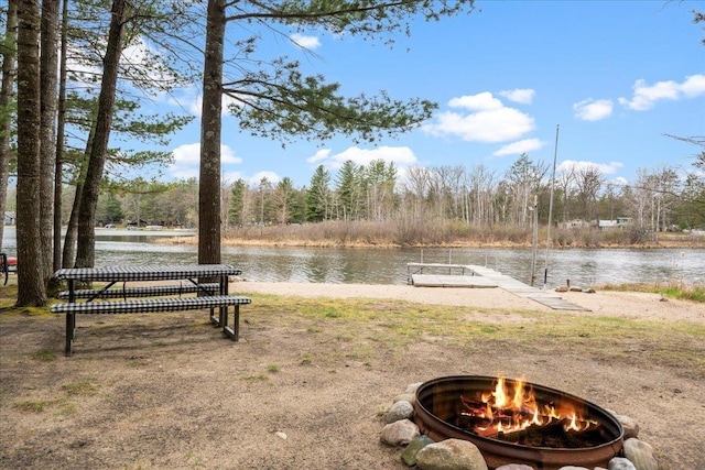 view of yard with an outdoor fire pit, a dock, a water view, and a view of trees