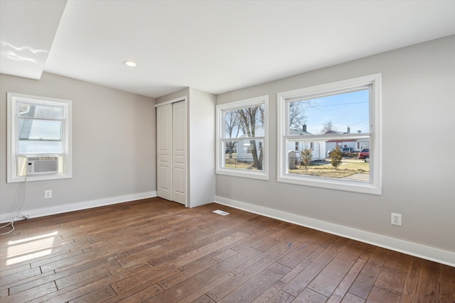 unfurnished bedroom featuring wood-type flooring, baseboards, multiple windows, and recessed lighting
