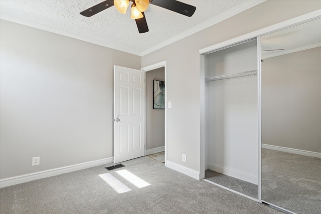 unfurnished bedroom with carpet floors, a textured ceiling, a closet, a ceiling fan, and crown molding