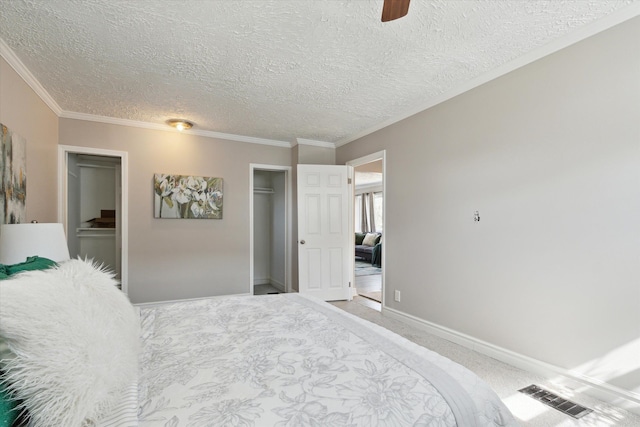 carpeted bedroom with a textured ceiling, crown molding, baseboards, a ceiling fan, and a closet