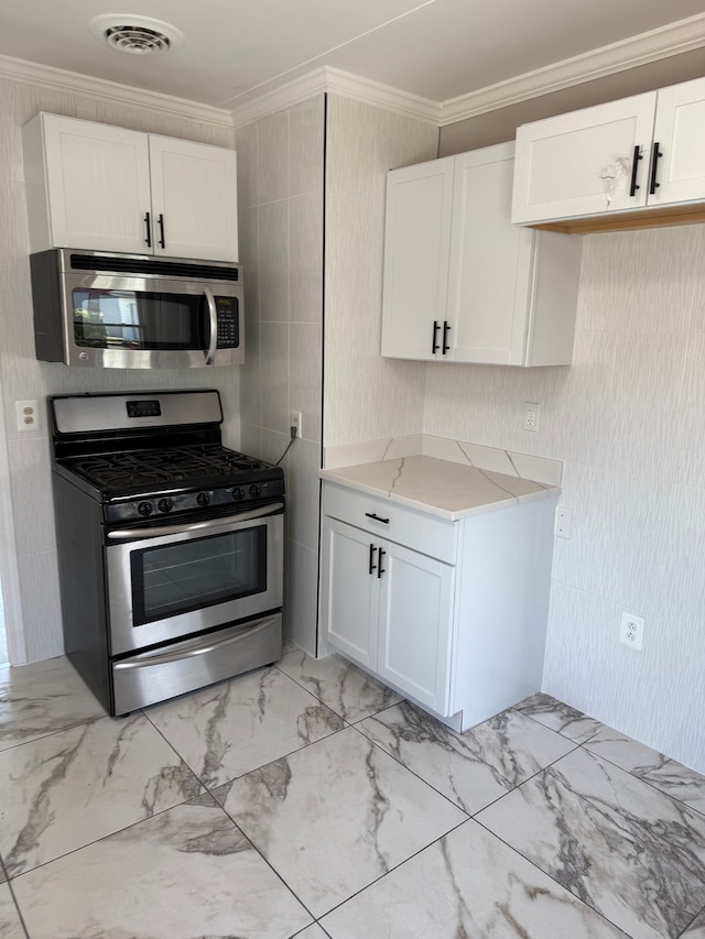 kitchen with stainless steel appliances, ornamental molding, white cabinets, light marble finish flooring, and light stone counters