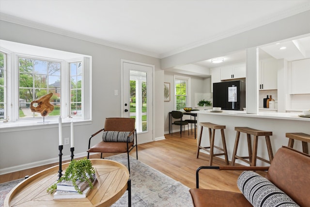 living area with light wood-type flooring, crown molding, and baseboards