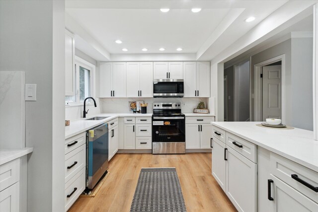kitchen with appliances with stainless steel finishes, a sink, white cabinetry, light wood-style flooring, and light countertops