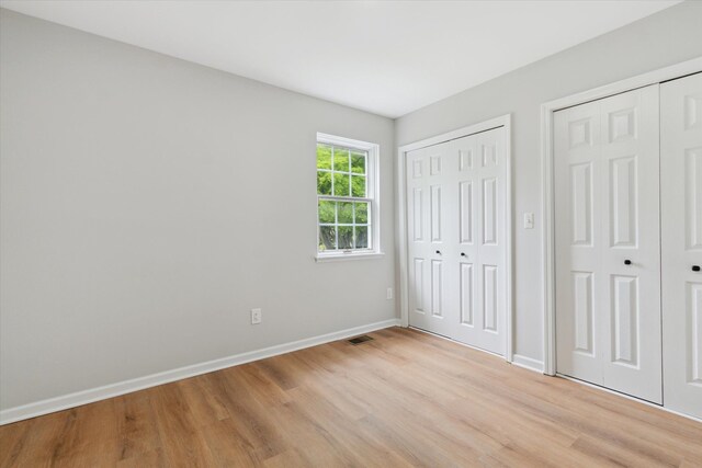 unfurnished bedroom featuring two closets, light wood-style floors, and baseboards