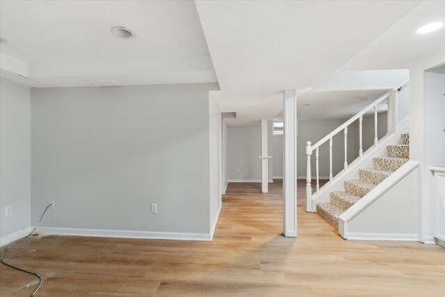 finished below grade area featuring stairway, wood finished floors, and baseboards