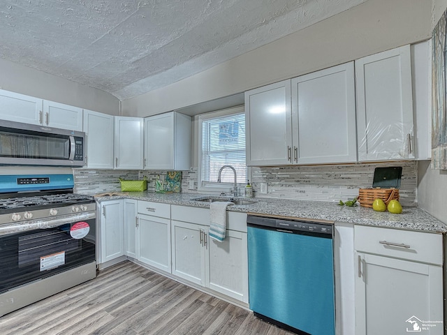 19106 Sylvia Ave, Romulus, MI 48174 - kitchen featuring appliances with stainless steel finishes, a sink, light wood-style flooring, decorative backsplash, and white cabinetry
