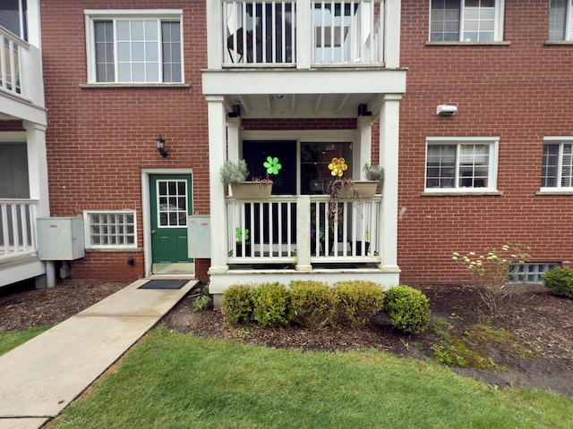 view of exterior entry with a balcony and brick siding