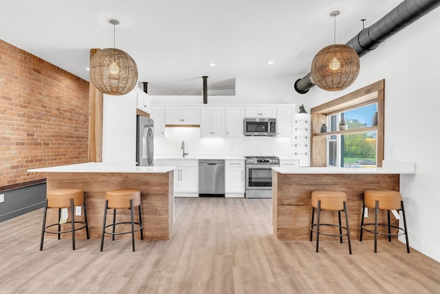 436 E Milwaukee St Unit 8, Detroit, MI 48202 - kitchen featuring appliances with stainless steel finishes, a peninsula, white cabinets, a breakfast bar, and brick wall