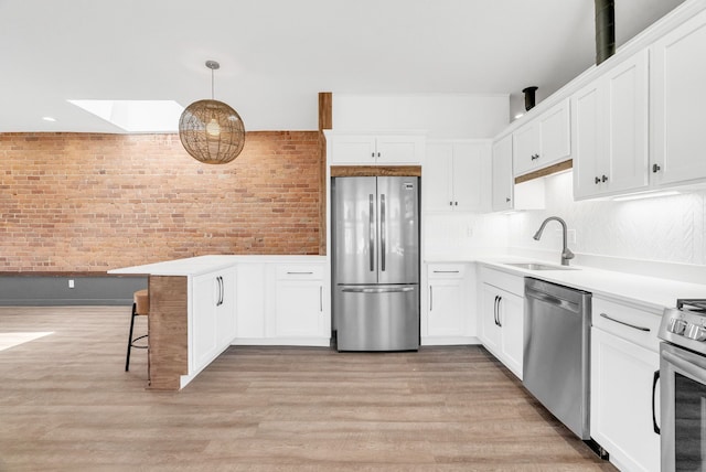 436 E Milwaukee St Unit 8, Detroit, MI 48202 - kitchen with stainless steel appliances, a sink, white cabinets, a peninsula, and brick wall