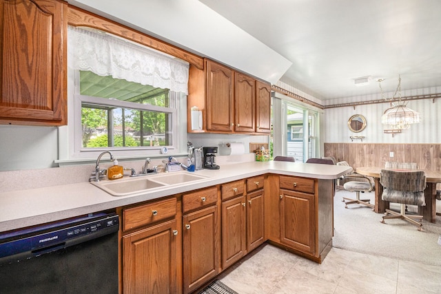 kitchen featuring black dishwasher, a sink, light countertops, brown cabinetry, and wainscoting