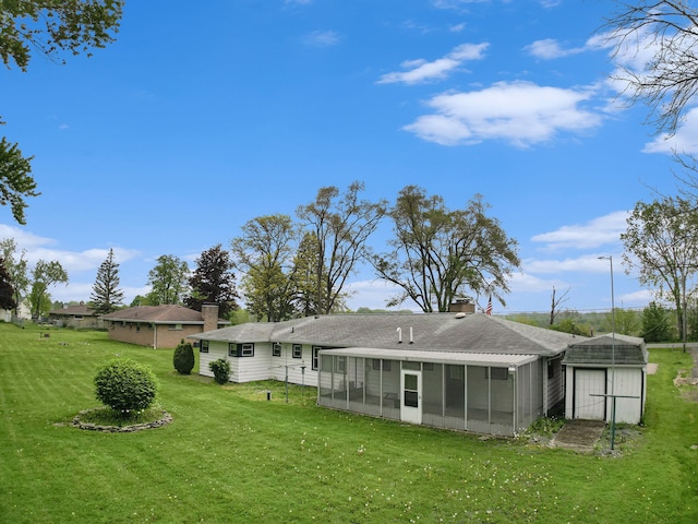 back of property featuring a sunroom, a yard, a chimney, a shingled roof, and a storage shed