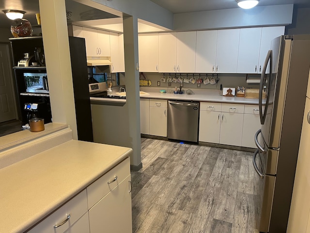 kitchen featuring stainless steel appliances, white cabinets, light wood-style floors, under cabinet range hood, and light countertops