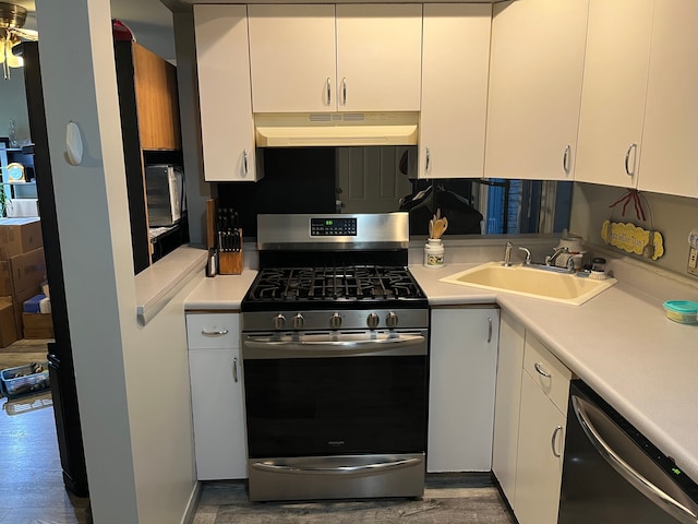 kitchen featuring under cabinet range hood, stainless steel appliances, a sink, light countertops, and white cabinetry
