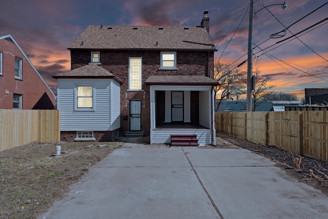 5027 Audubon Rd, Detroit, MI 48224 - back of house at dusk with a chimney, a fenced backyard, brick siding, and a shingled roof