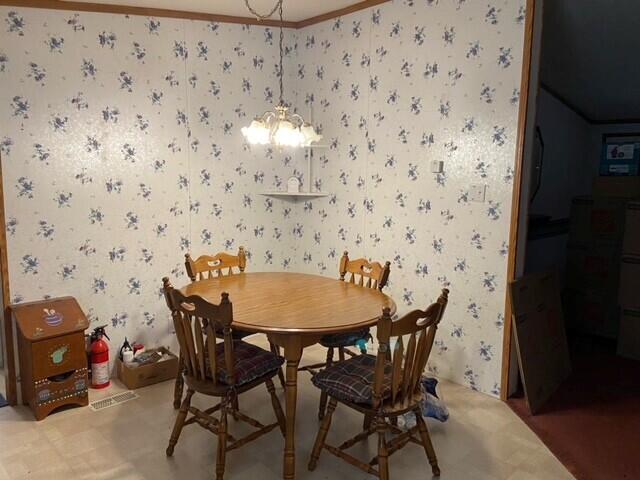 dining area featuring wallpapered walls, ornamental molding, and a chandelier
