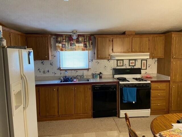 kitchen featuring white appliances, under cabinet range hood, a sink, and brown cabinetry