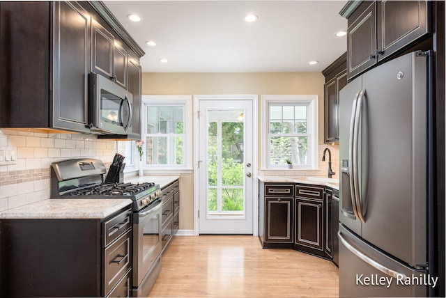 kitchen with appliances with stainless steel finishes, a sink, light wood-style flooring, dark brown cabinets, and recessed lighting