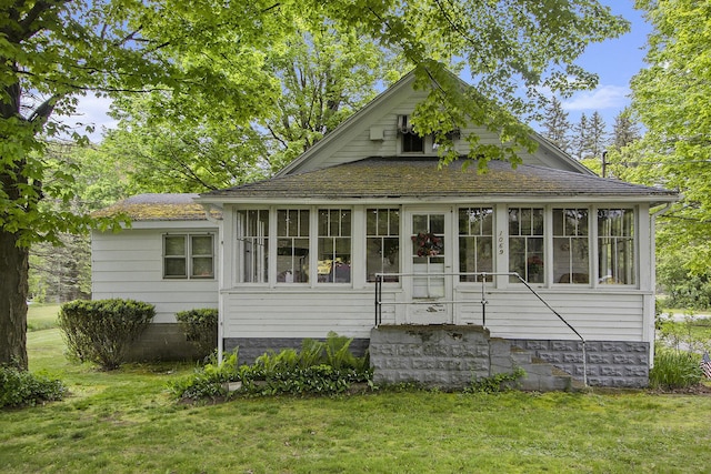 view of front facade featuring a sunroom, a front yard, and roof with shingles