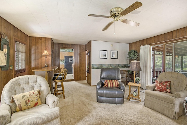 living area featuring wooden walls, light carpet, and a ceiling fan