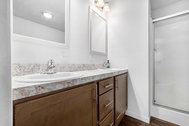 bathroom with a stall shower, wood finished floors, double vanity, and baseboards