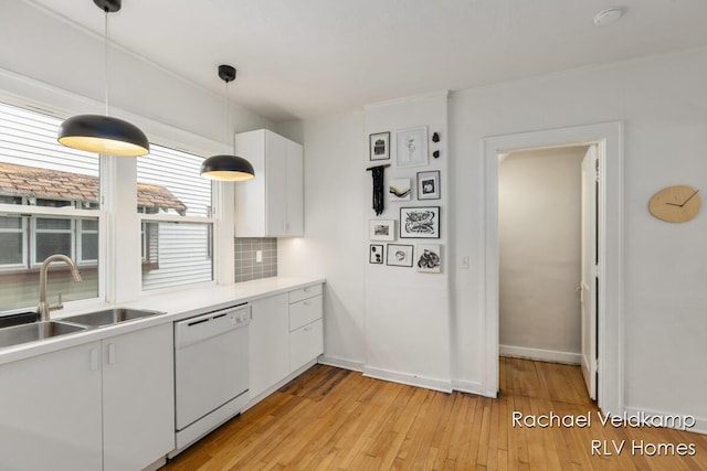kitchen featuring white dishwasher, a sink, white cabinets, light wood-style floors, and light countertops